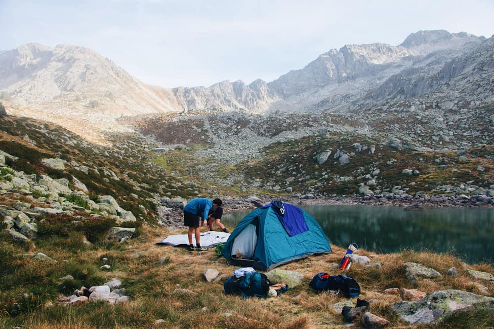 A tent beside a mountain lake with peaks behind it