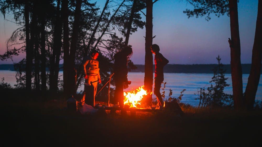 Friends around a campfire beside a lake at twilight