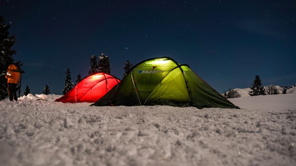 Two lit tents on snow under a starry sky