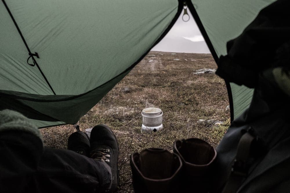 The view from a tent toward someone cooking outdoors