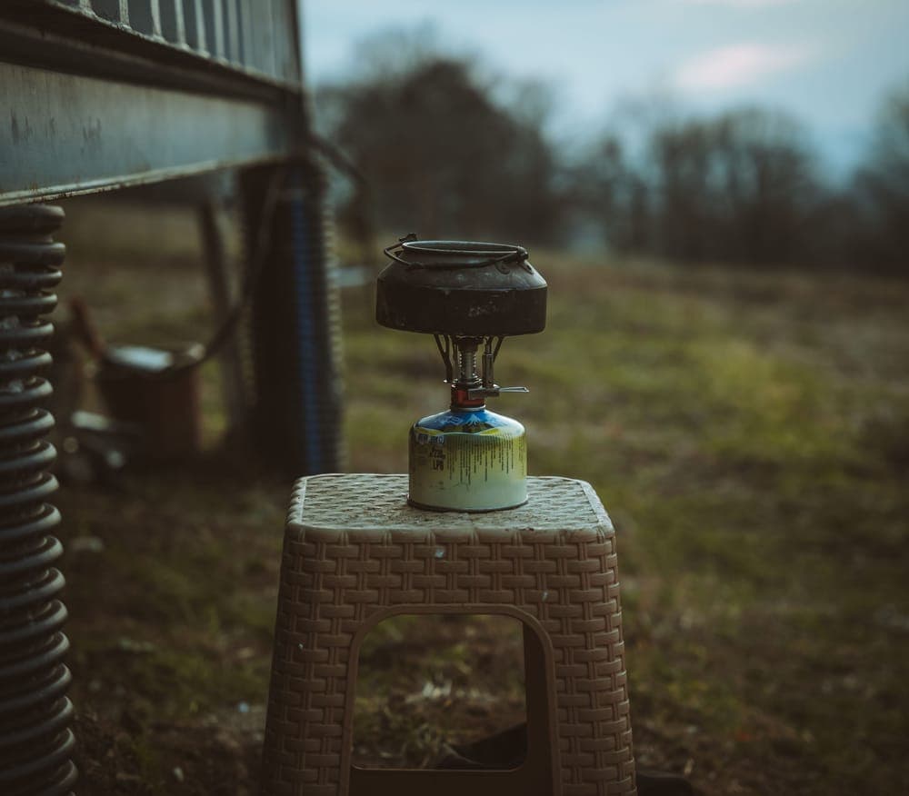 A small camping stove set on a stool in an open field
